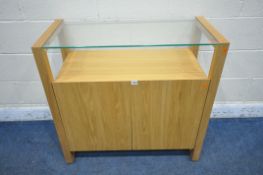A SOLID LIGHT OAK SIDE TABLE, with a glass top, above two cupboard doors, width 90cm x depth 42cm