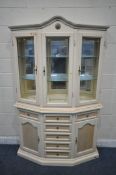 A 20TH CENTURY CREAM PAINTED CANTED DISPLAY CABINET, the top with an arched crest, three doors
