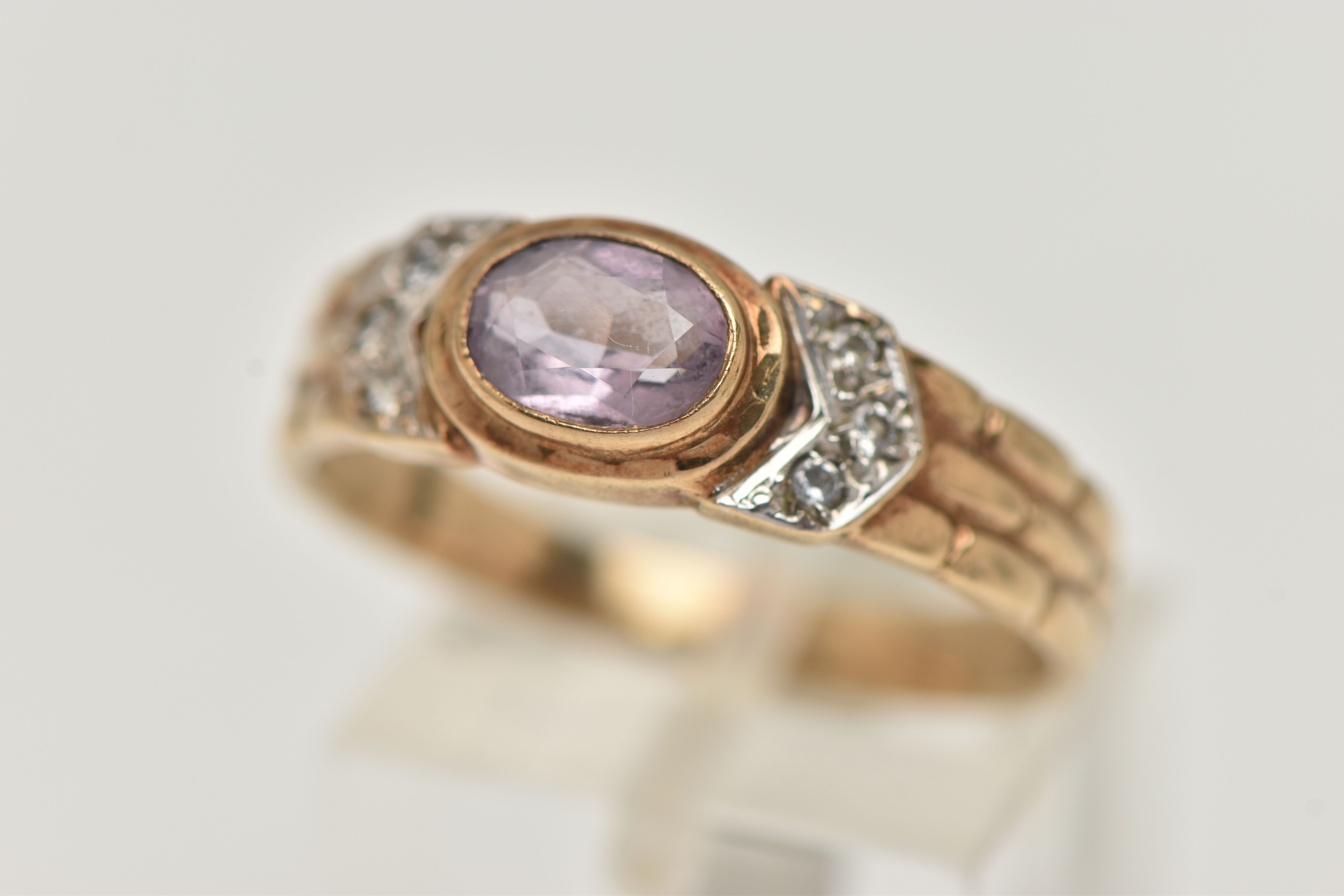 A 9CT GOLD AMETHYST RING, the central oval amethyst in a collet setting, flanked by colourless