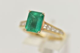A YELLOW METAL EMERALD AND DIAMOND RING, centering on an emerald cut emerald, measuring