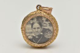 A YELLOW METAL MEMORIAL PHOTO PENDANT, a circular form pendant with embossed detail, encasing a