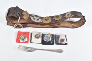 A COLLECTION OF CAP BADGES ON A LEATHER BELT, a WWII fork and some football medals, the belt has