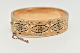 A YELLOW METAL HINGED BANGLE, wide bangle decorated with a black enamel pattern with textured