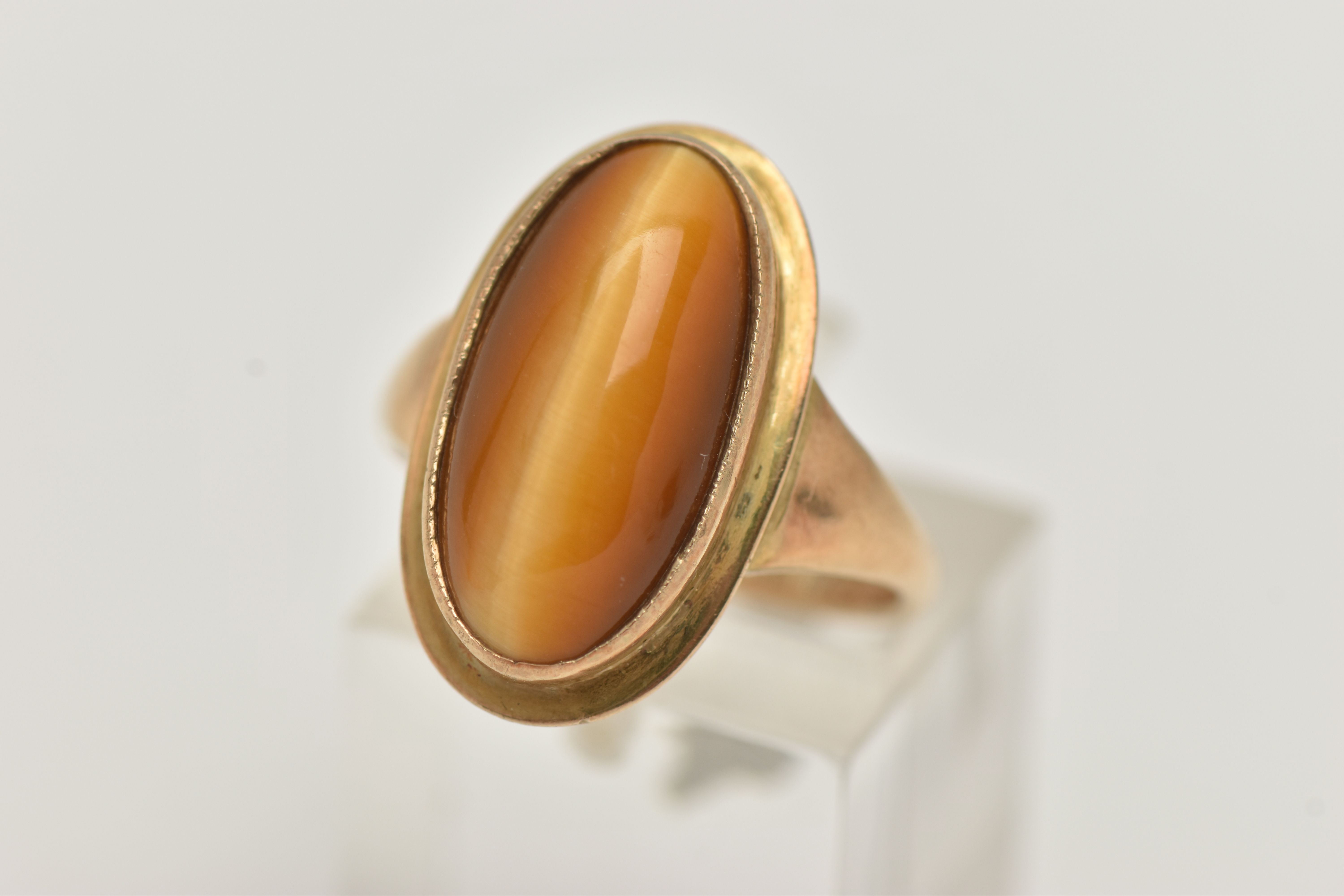A 9CT GOLD DRESS RING, an elongated oval cabochon tigers eye, collet set in yellow gold, leading