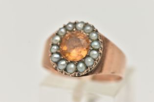 A ROSE METAL CLUSTER RING, centering on an oval cut orange topaz within a surround of split