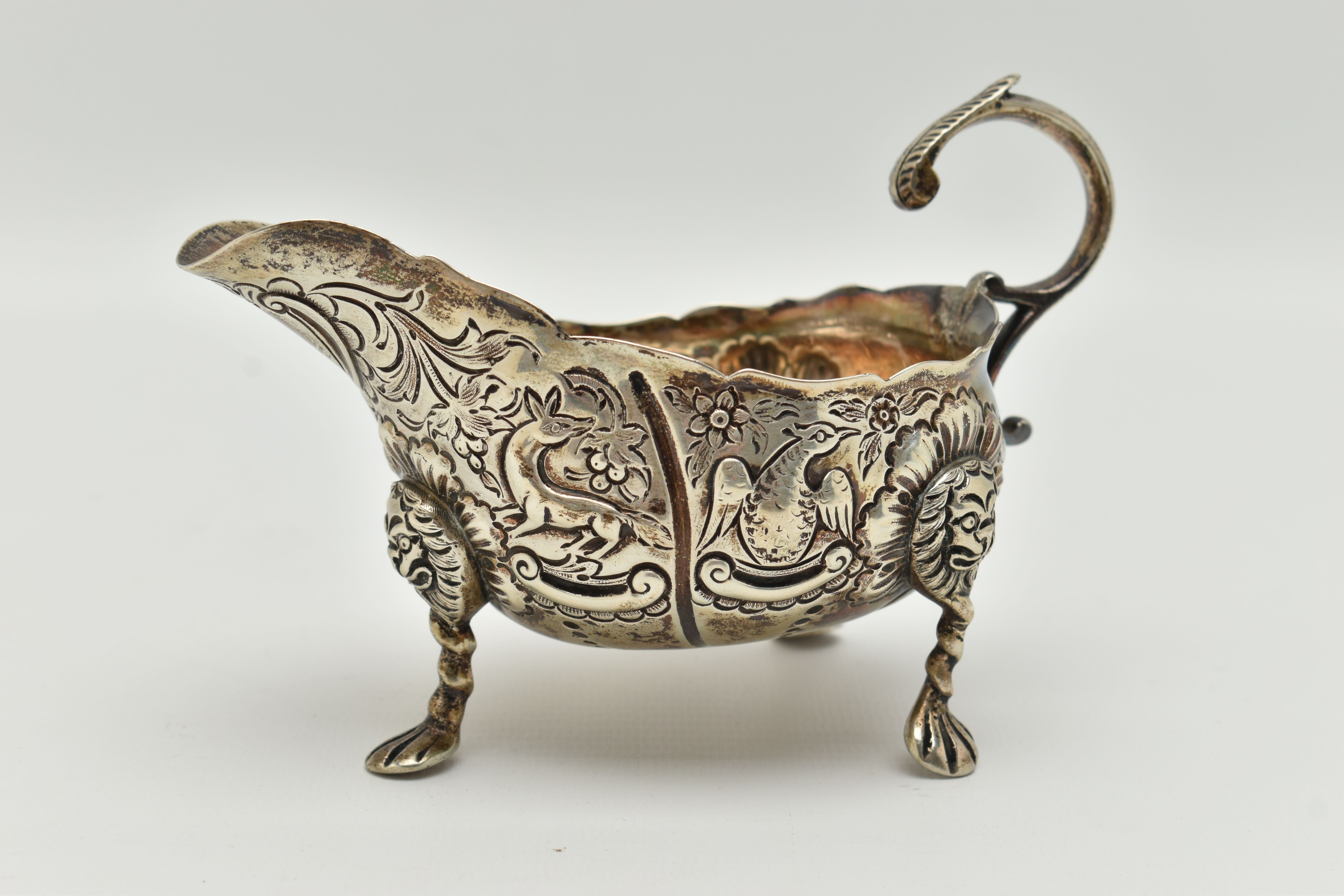 AN IRISH SILVER GRAVY BOAT, early 20th century, embossed animal and floral pattern, with three