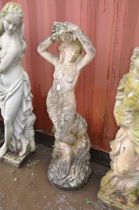 A WEATHERED COMPOSITE FIGURE OF A SCANTILY CLAD LADY leaning against a low wall and placing a laurel