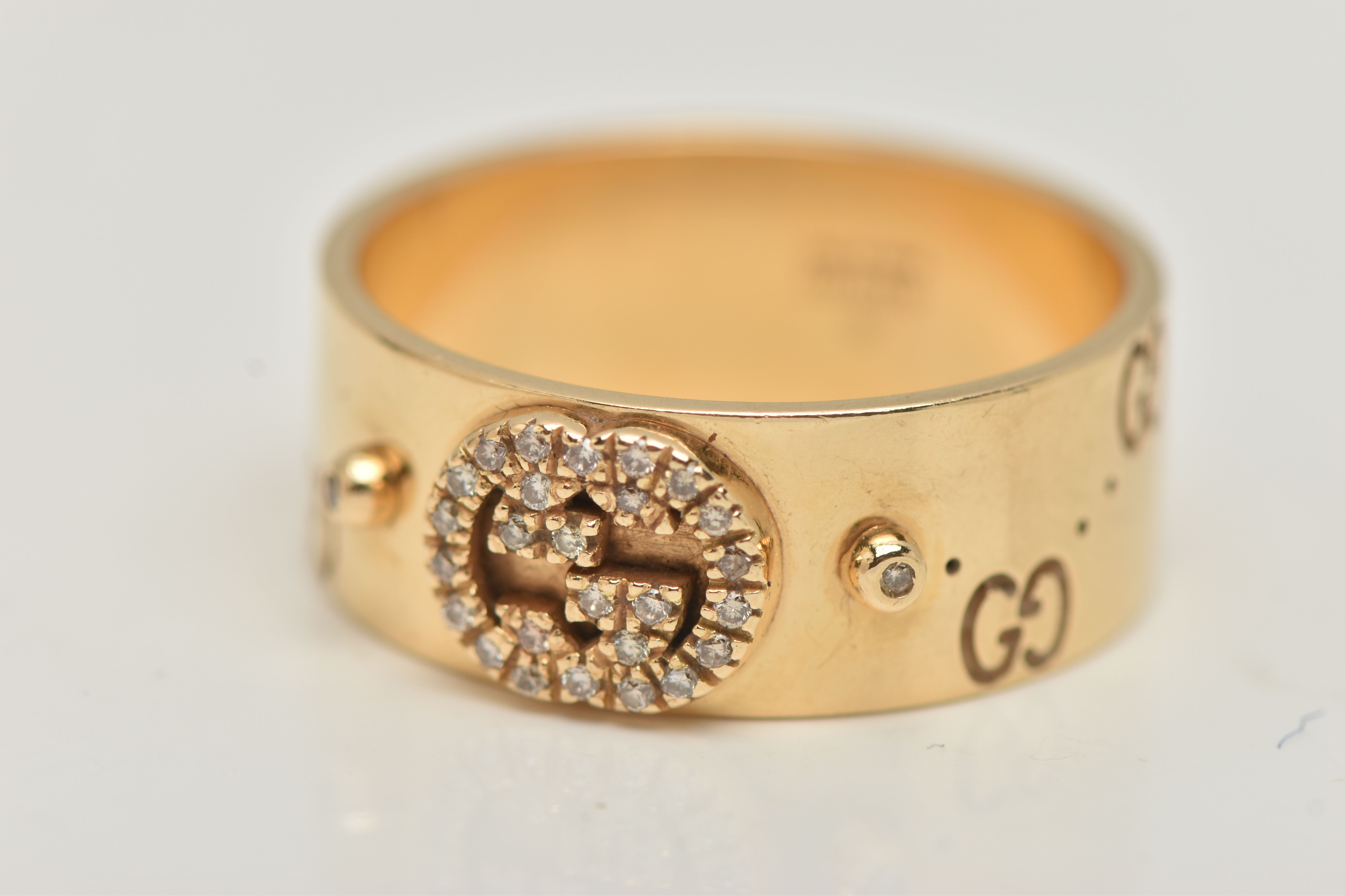 AN 18CT GOLD 'GUCCI' ICON BAND RING, a wide yellow metal band with a repetitive 'Gucci' logo and a