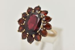 A GARNET CLUSTER RING, designed as a central oval garnet within an oval garnet surround, in claw