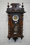 A 20TH CENTURY MAHOGANY VIENNA WALL CLOCK, twin finials flanking a mask, the arched glass door