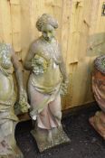 A WEATHERED COMPOSITE GARDEN FIGURE in the form of a Roman lady resting by a tree stump holding
