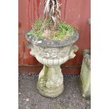 A WEATHERED COMPOSITE GARDEN URN ON STAND with a circular tapering stand , acanthus leaf detail