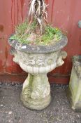 A WEATHERED COMPOSITE GARDEN URN ON STAND with a circular tapering stand , acanthus leaf detail
