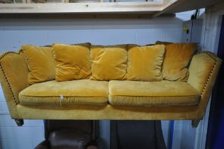 A GOLD VELOUR UPHOLSTERED SOFA, with a studded back, sides, and a shaped top, on square light oak