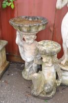 TWO WEATHERED COMPOSITE GARDEN FIGURES DEPICTING PUTTI one seated resting a bowl on its head (some