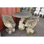 A WEATHERED COMPOSITE GARDEN TABLE AND THREE SIMILAR CHAIRS, the table is in the form of a crouching