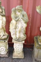 A WEATHERED COMPOSITE GARDEN FIGURE of embracing lovers standing on a ornately decorated base