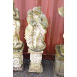 A WEATHERED COMPOSITE GARDEN FIGURE of embracing lovers standing on a ornately decorated base