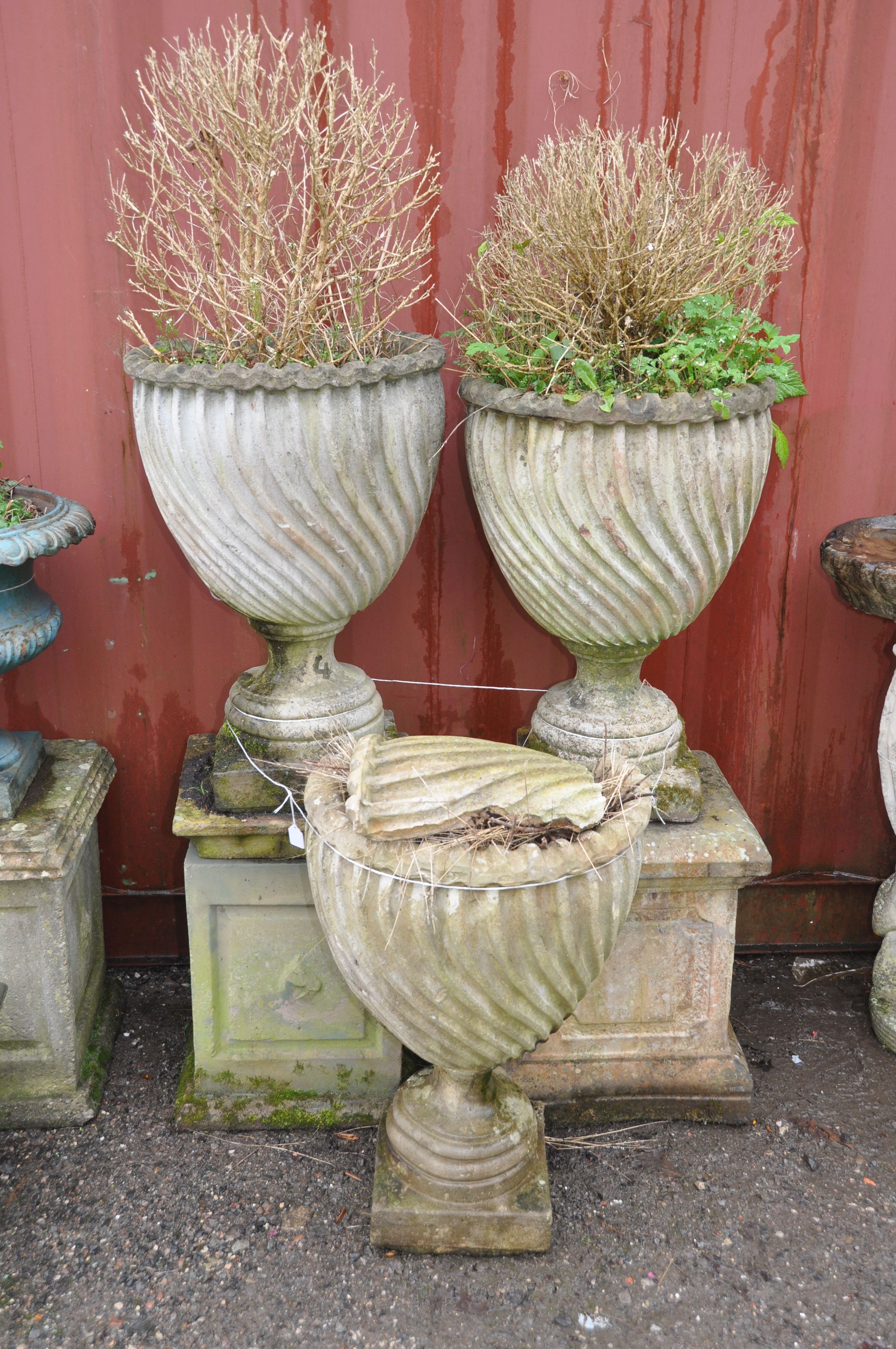 A PAIR OF WEATHERED COMPOSITE SPIRAL FLUTED GARDEN URNS mounted on two different square bases and