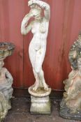 A WEATHERED COMPOSITE GARDEN FIGURE OF A STANDING CLAD LADY attending to her hair standing on a