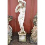 A WEATHERED COMPOSITE GARDEN FIGURE OF A STANDING CLAD LADY attending to her hair standing on a