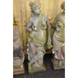 A WEATHERED COMPOSITE GARDEN FIGURE in the form of a Roman lady resting by a tree stump holding