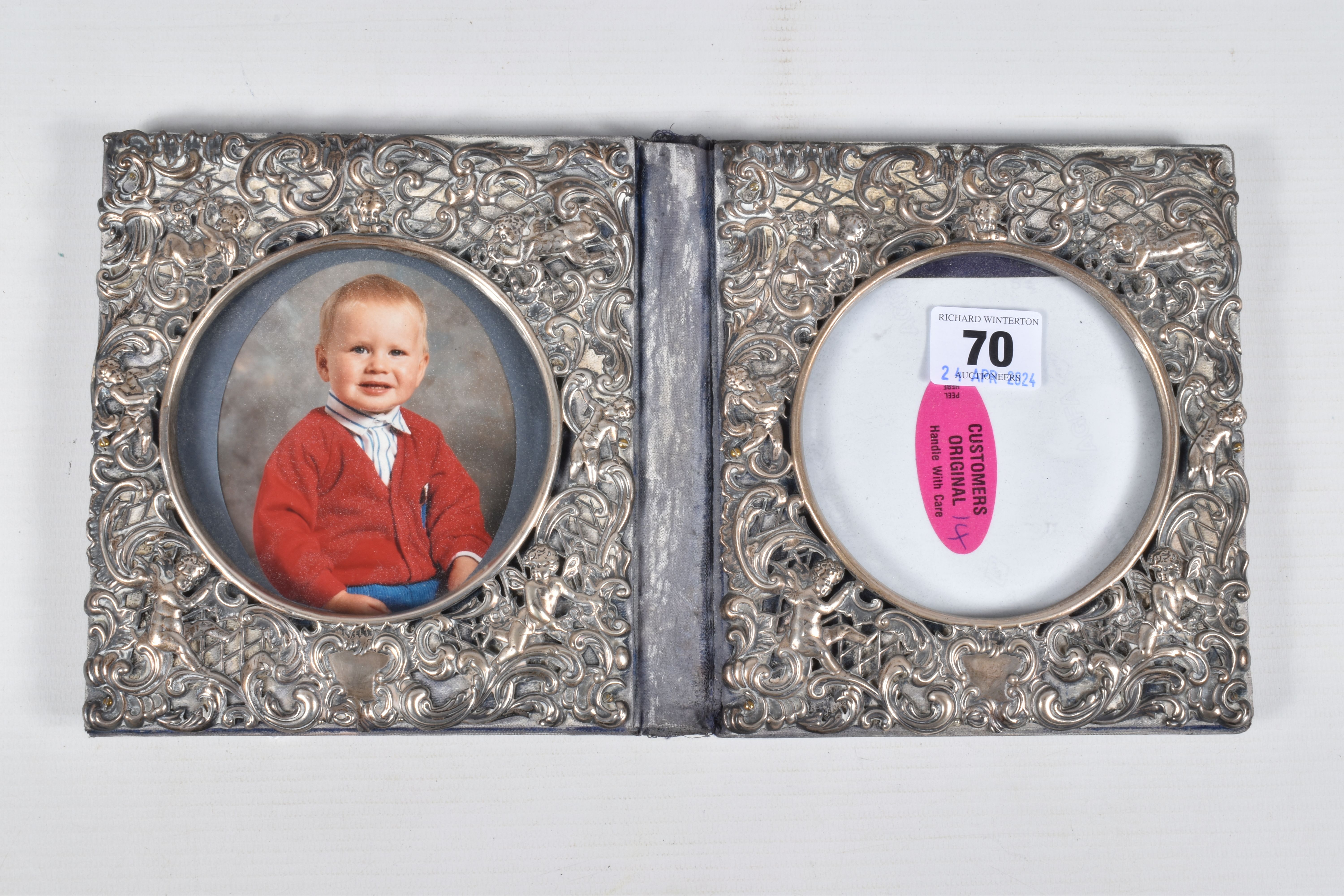 A DOUBLE PHOTO FRAME, white metal lined frame, with embossed foliate pattern with cherubs, folding