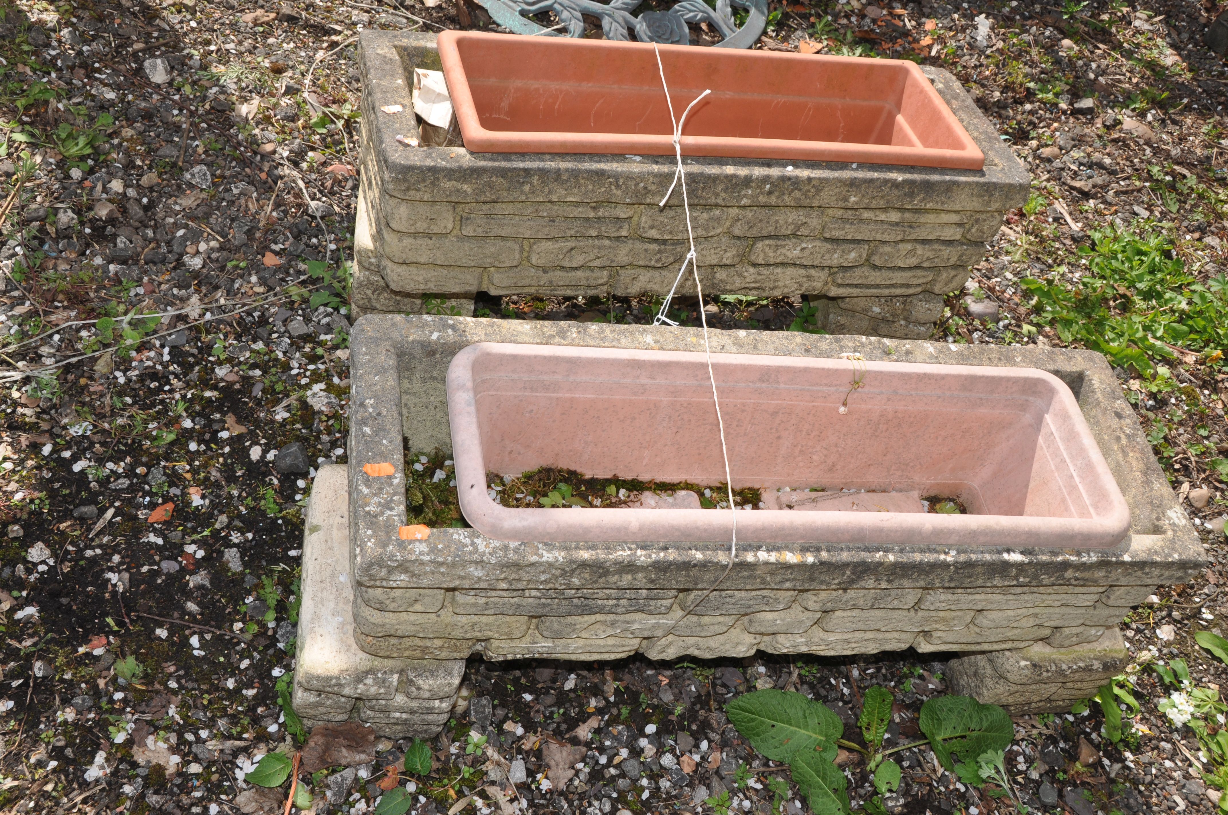 A PAIR OF WEATHERED COMPOSITE RECTANGULAR BRICK EFFECT PLANTERS with matching bases and plastic