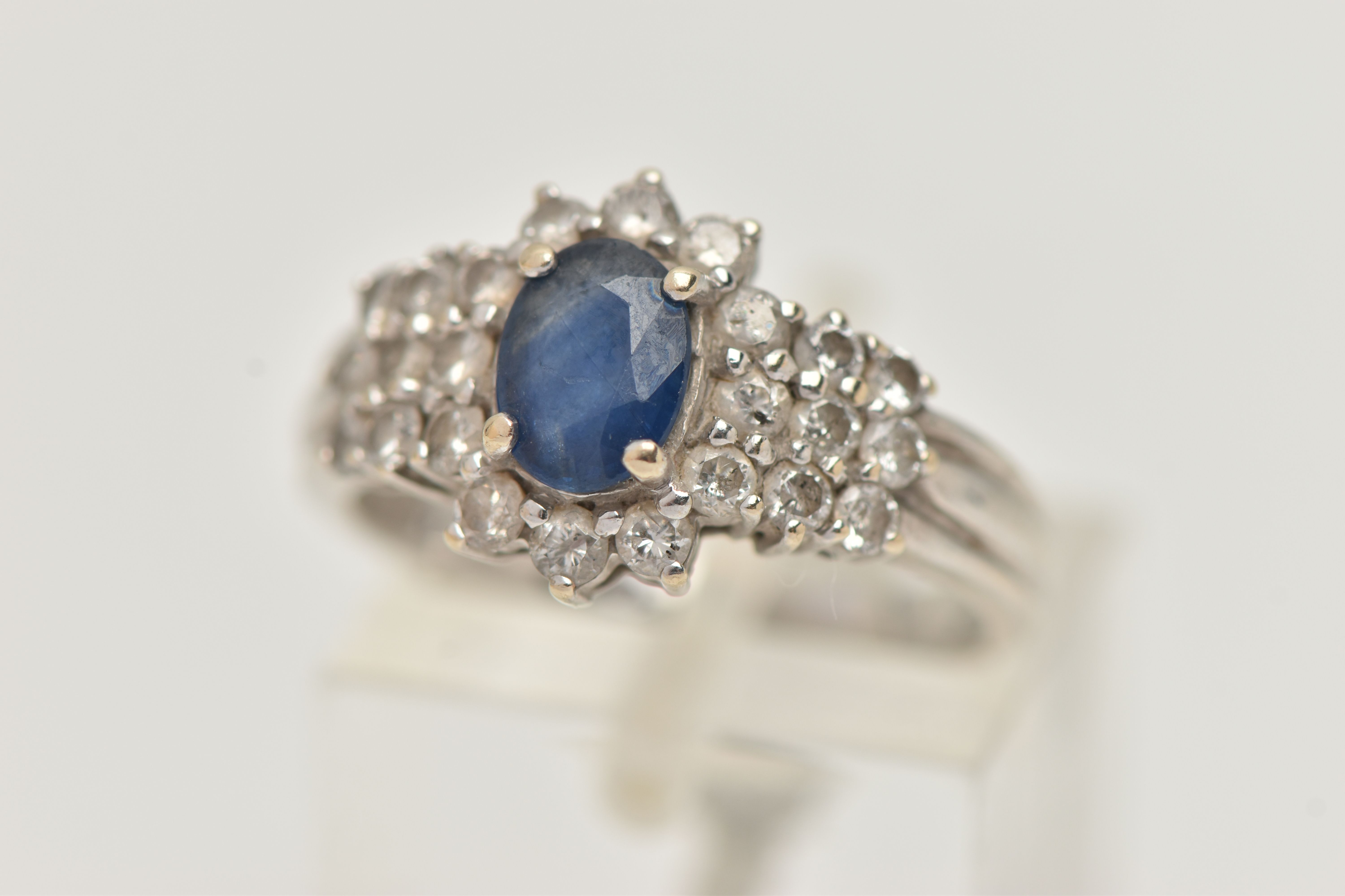 AN 18CT WHITE GOLD SAPPHIRE AND DIAMOND CLUSTER RING, centrally set with an oval cut blue