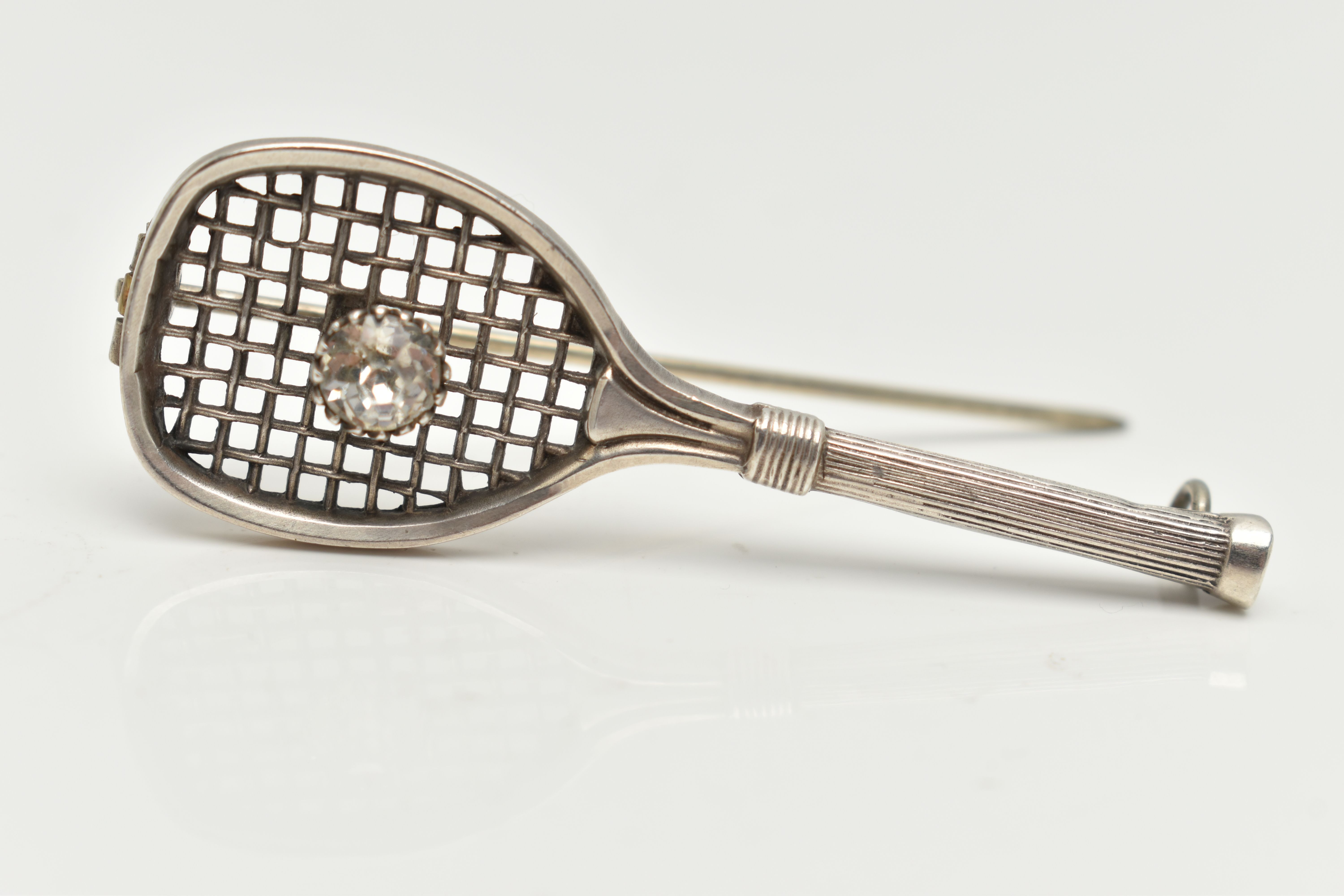 A WHITE METAL BROOCH, in the form of a tennis racket set with a colourless paste imitating a