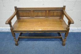 AN OLD CHARM OAK SETTLE, with three linenfold panels, open armrests, raised on block and turned