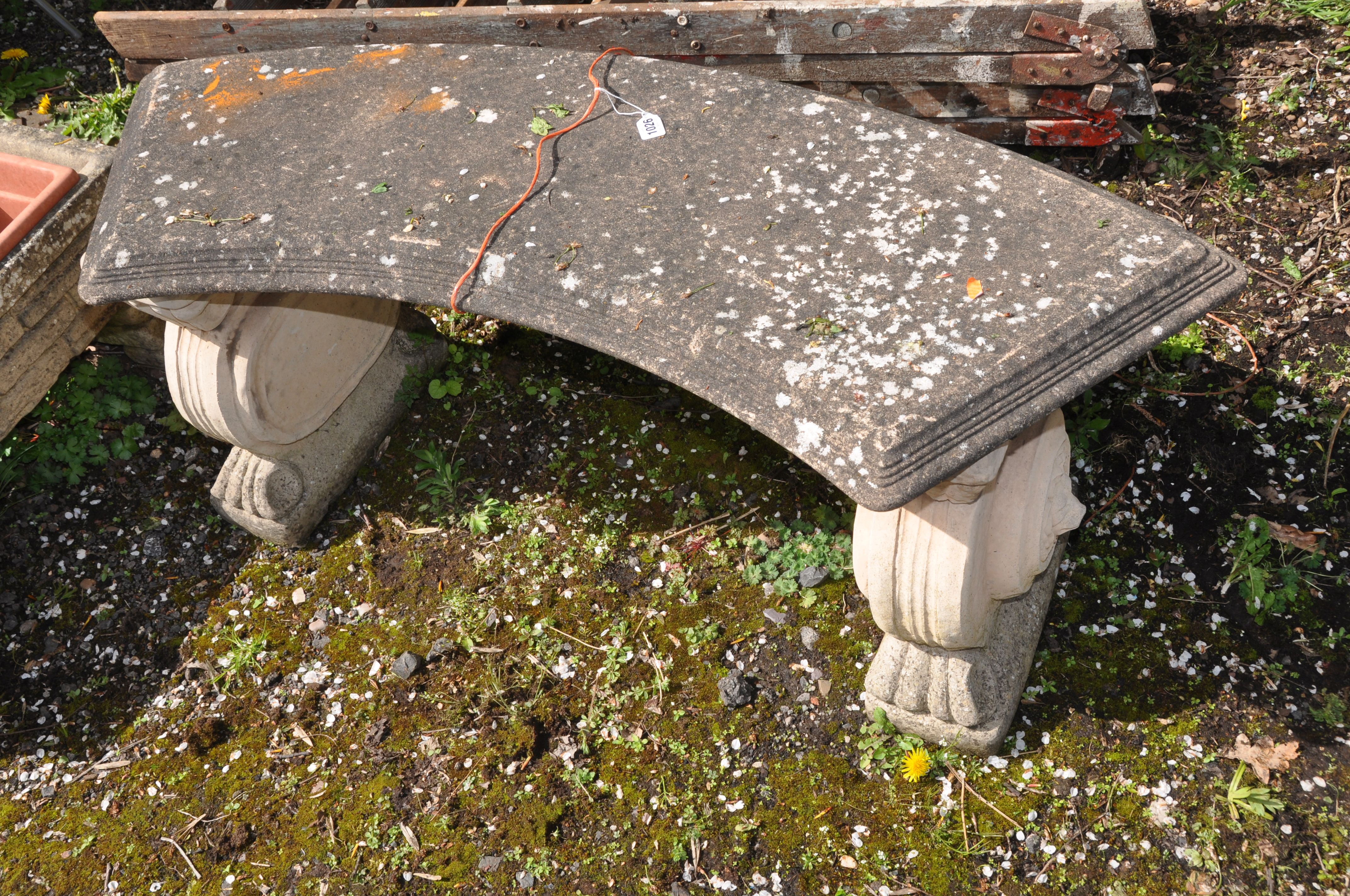 A WEATHERED COMPOSITE CURVED GARDEN BENCH with lion head motifs to each base 123cm long (condition