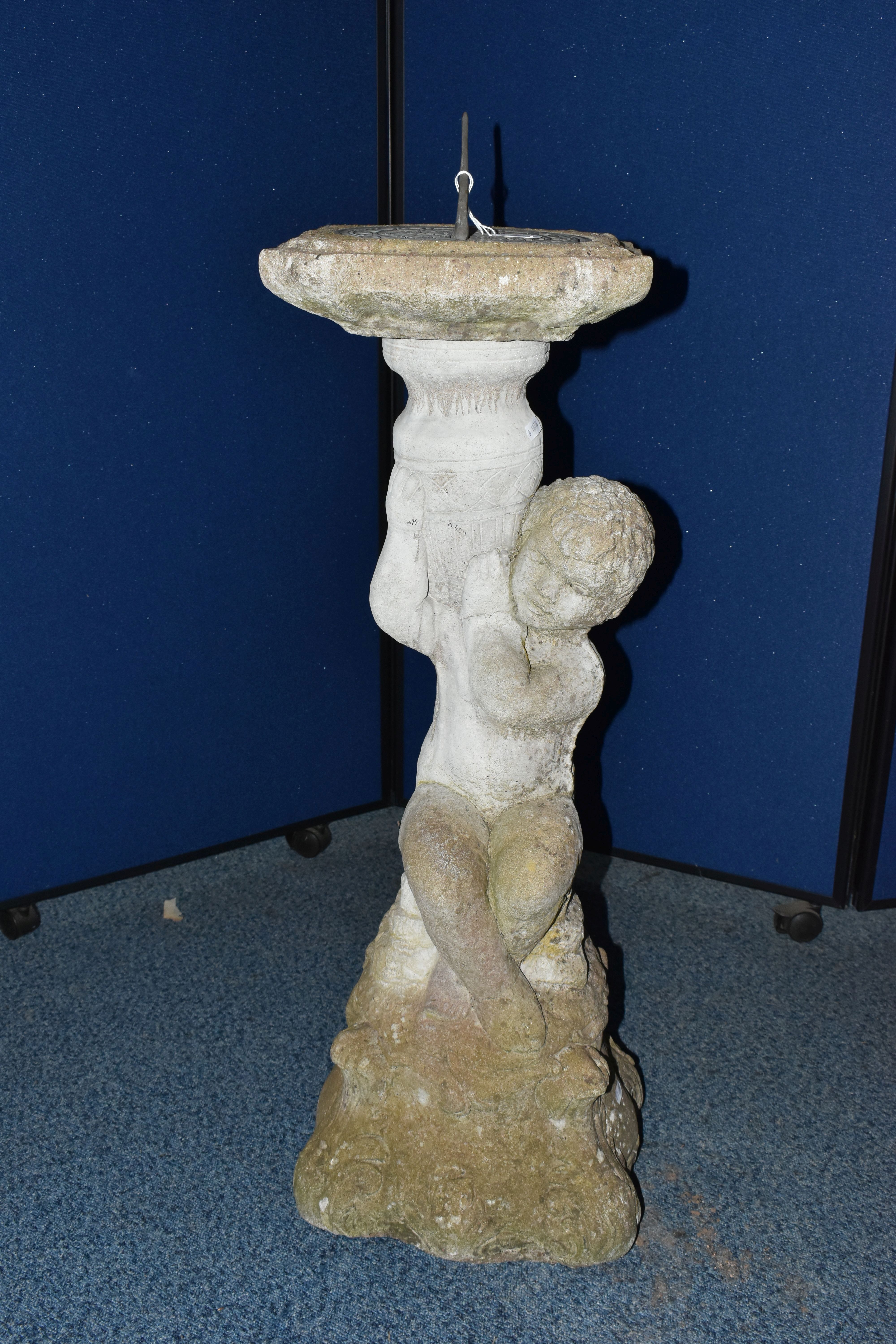 A WEATHERED COMPOSITE SUN DIAL, the top is raised on a seated putti holding an urn aloft, diameter