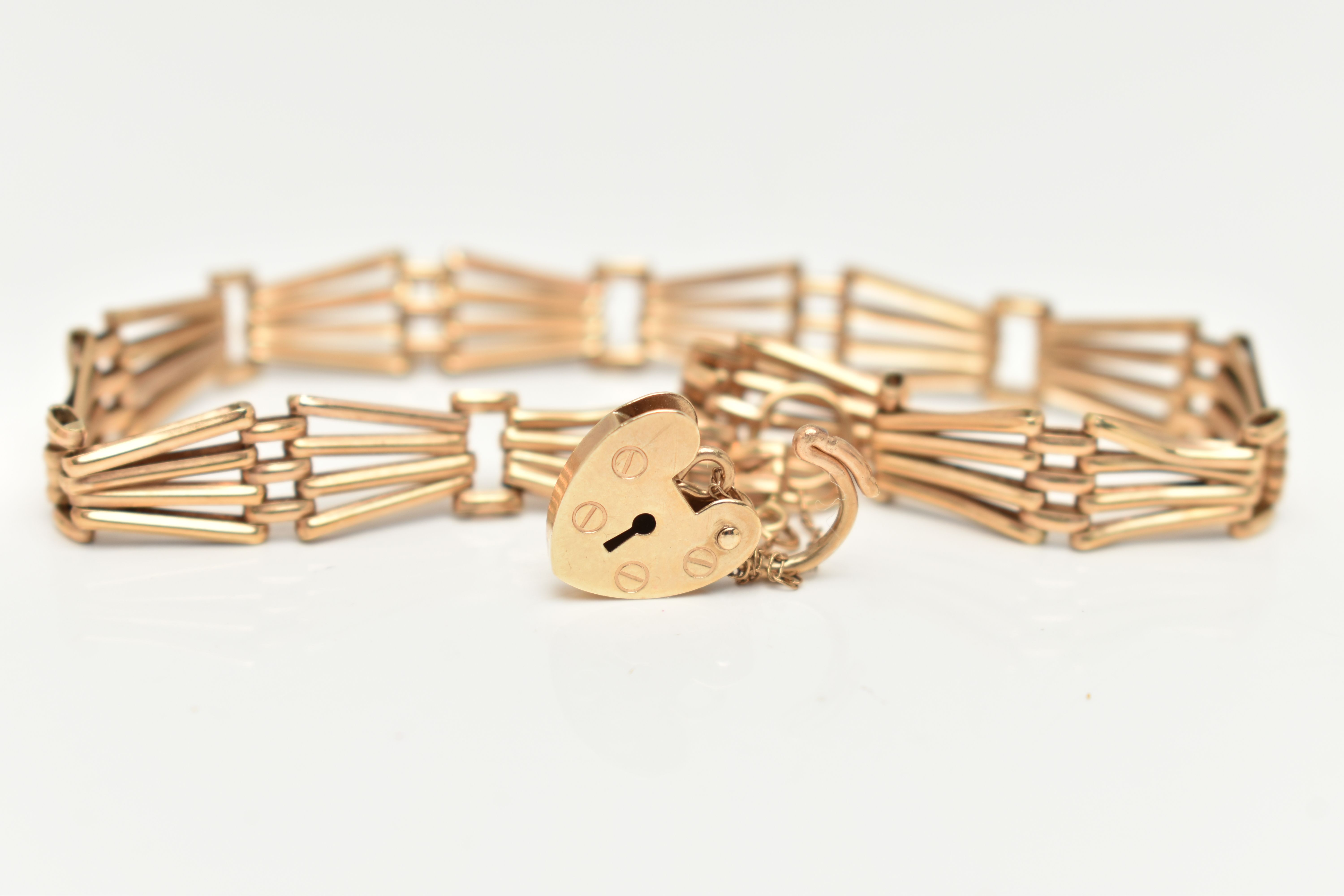 A 9CT YELLOW GOLD BRACELET WITH PADLOCK CLASP, the plain polished abstract design four row gate