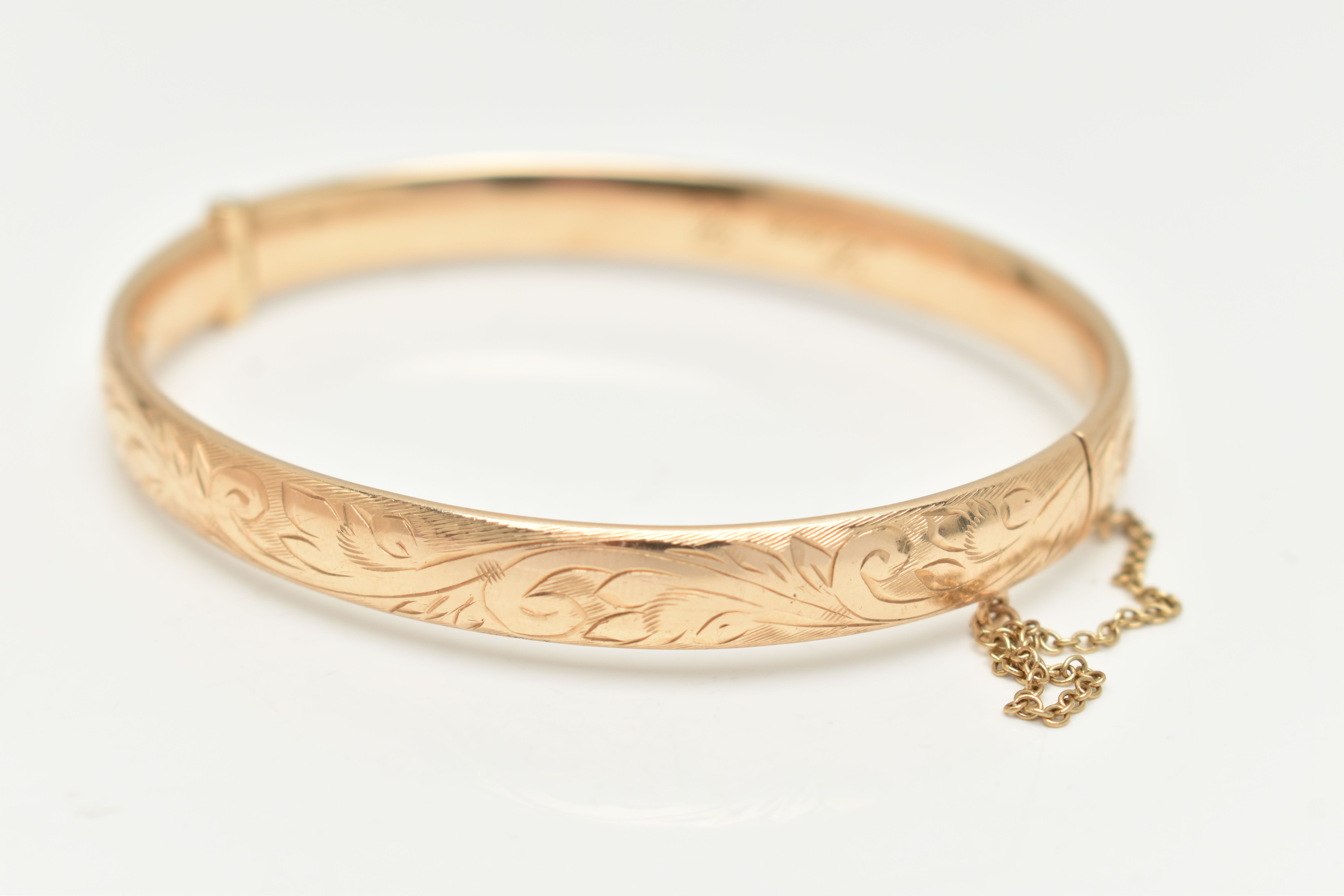 A 9CT GOLD HINGED BANGLE, with engraved scrolling acanthus decoration throughout to the hidden