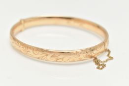 A 9CT GOLD HINGED BANGLE, with engraved scrolling acanthus decoration throughout to the hidden