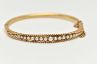 A LATE 19TH CENTURY YELLOW METAL BANGLE, hinged oval bangle, set with twenty one graduated seed