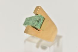 A YELLOW METAL GEM SET DRESS RING, designed with a tapered slice of green hardstone, between two