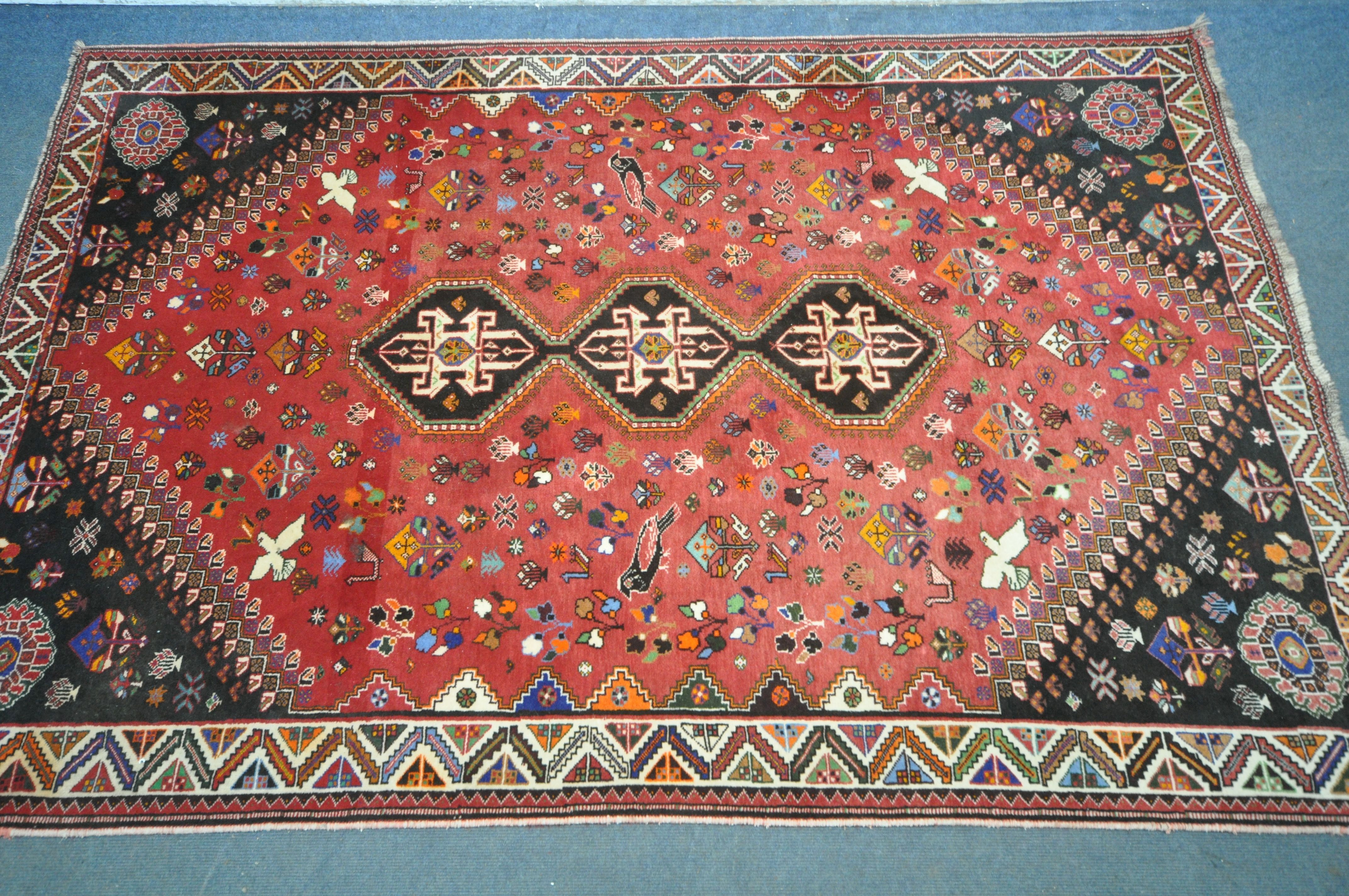 A WOOLLEN RED GROUND RUG, with a repeating pattern of birds, three central medallions, black