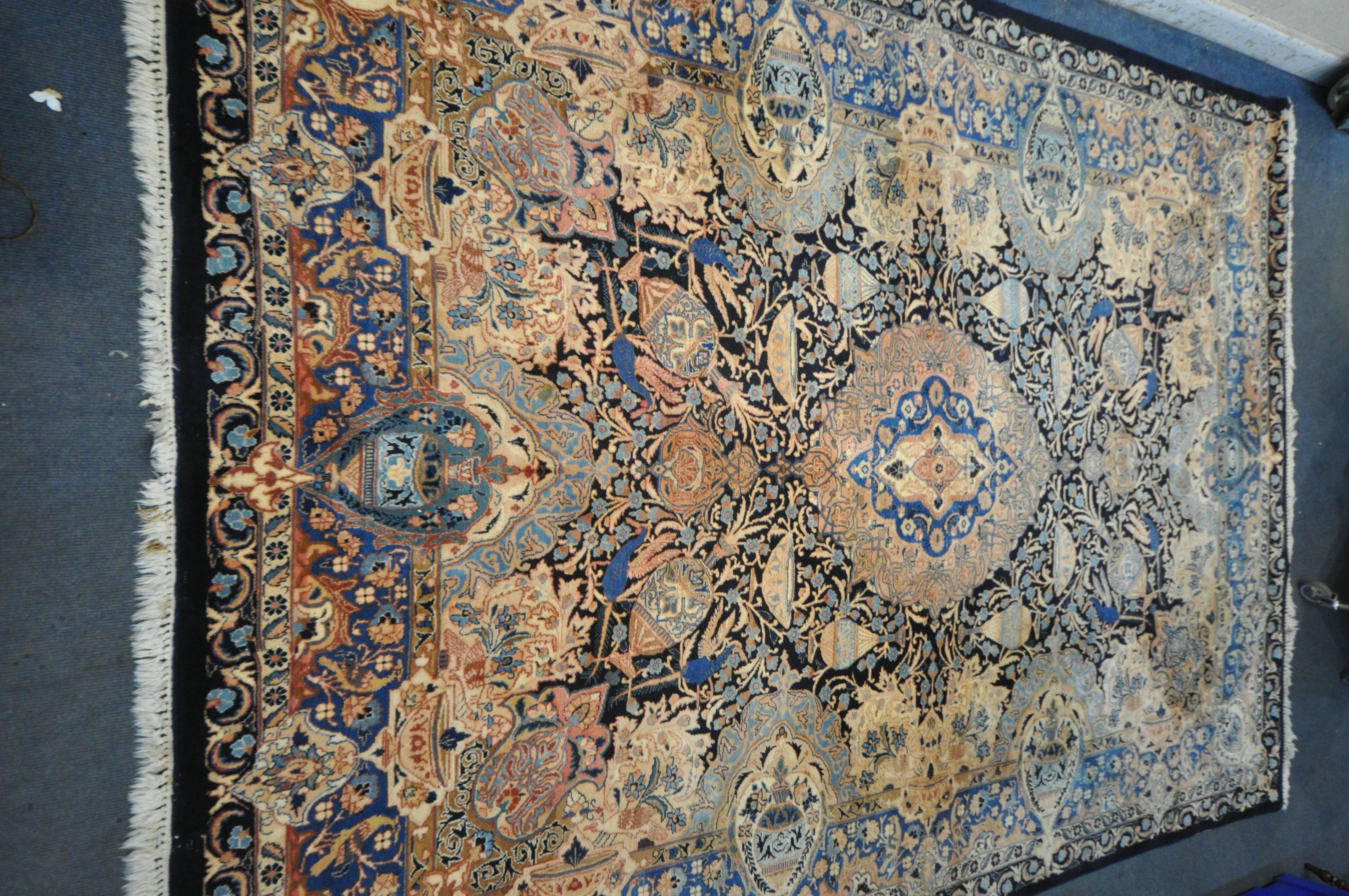 A LARGE WOOLLEN CREAM GROUND RUG, with a repeating foliate pattern, within a dark blue field, and