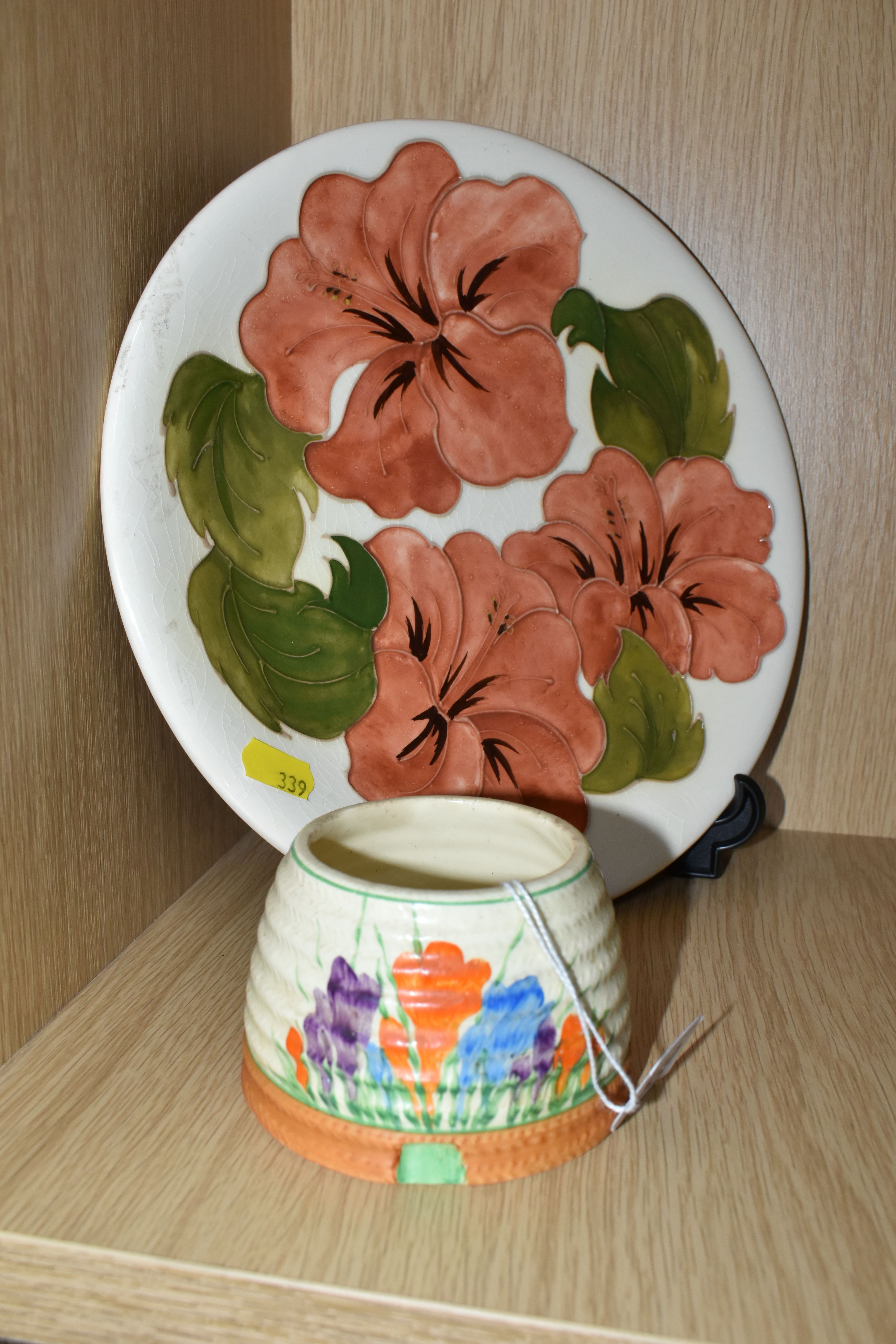 A MOORCROFT POTTERY 'HIBISCUS' PATTERNED PLATE AND A CLARICE CLIFF SUGAR BOWL, comprising a coral