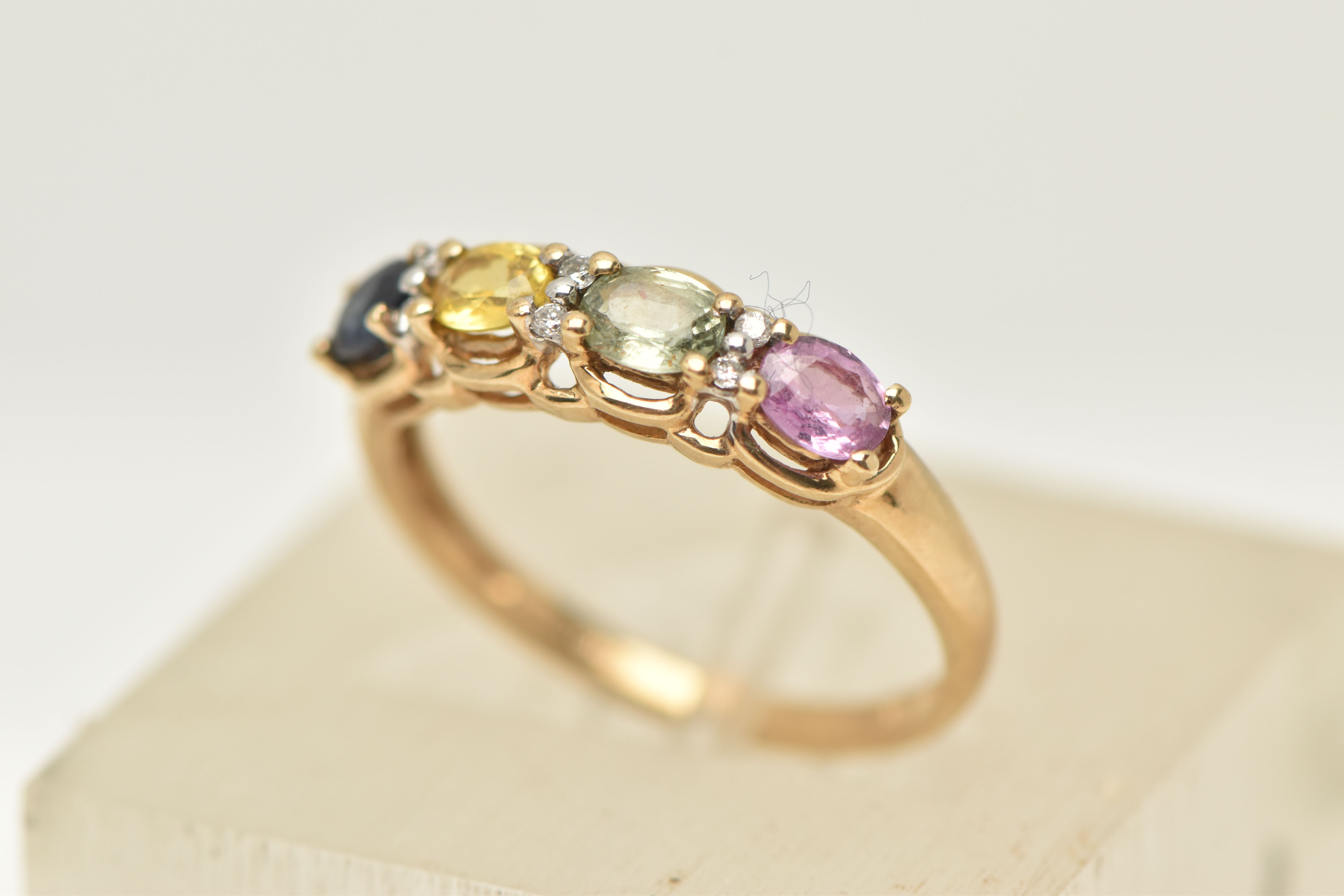 A 9CT GOLD MULTI-GEM RING, designed as a line of four oval gems to include sapphire and topaz,