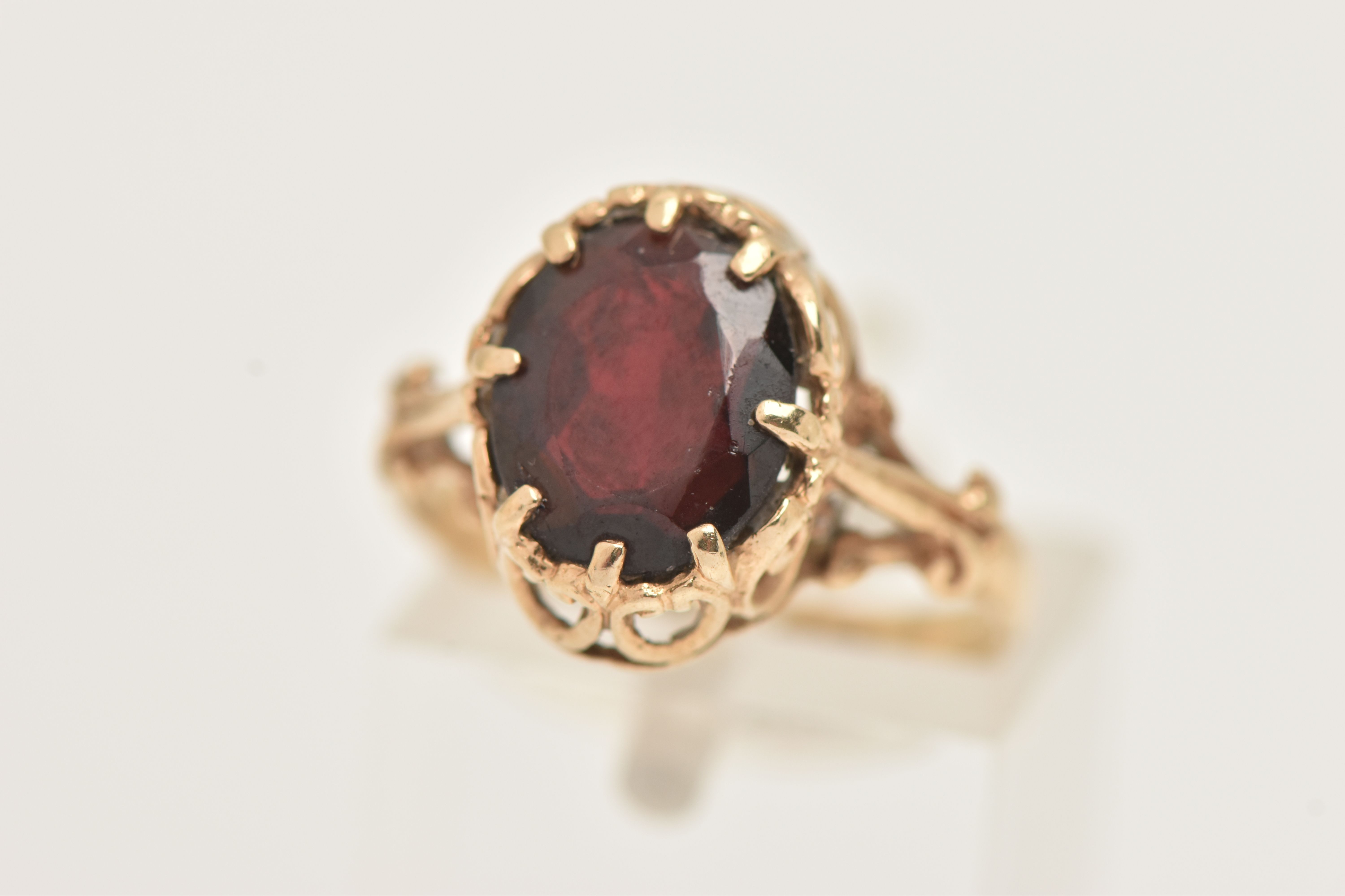 A 9CT GOLD GARNET RING, the oval garnet in an eight claw setting, to the scrolling gallery and