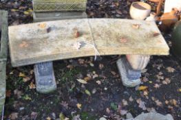 A WEATHERED COMPOSITE CURVED GARDEN BENCH, with painted bases adorned with Fleur de lis, and similar