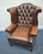 A TANNED BUTTONED LEATHER CHESTERFIELD WINGBACK ARMCHAIR, with scrolled armrests, raised on front