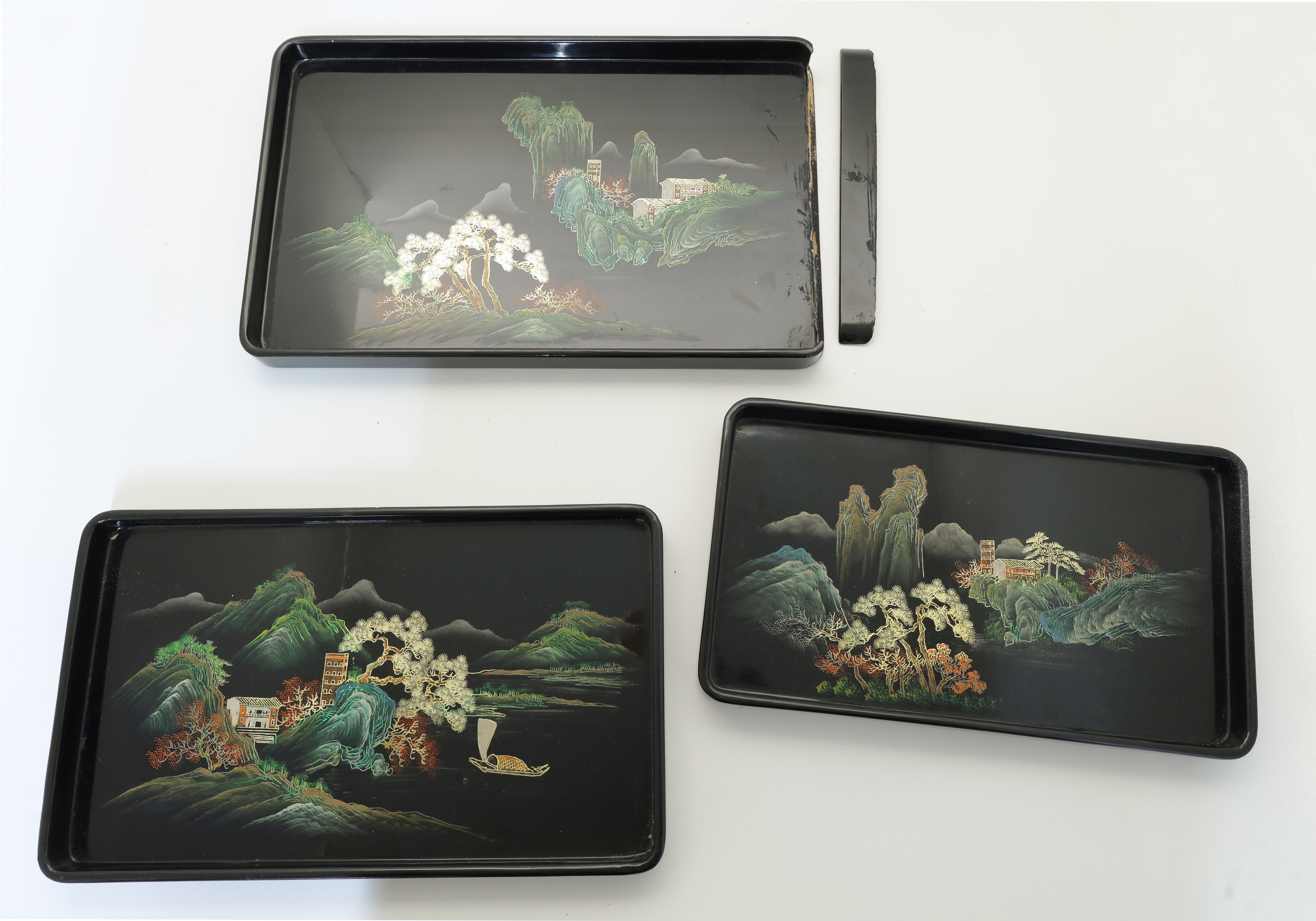 A set of three graduated black lacquer trays, 20th century, each painted with a Chinoiserie lands...