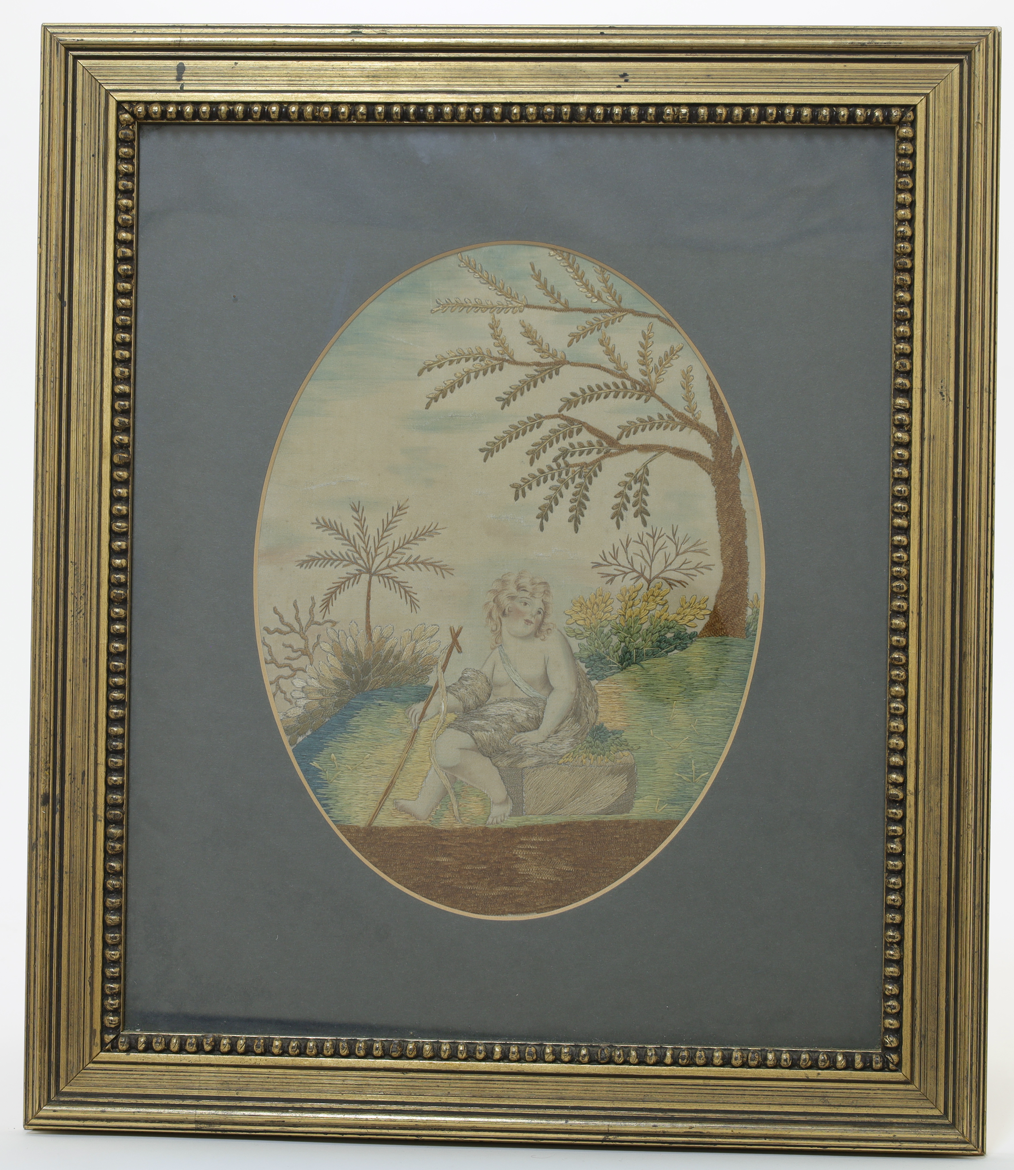 A George III oval silk embroidery, depicting the young Christ seated on a rock within a landscape...