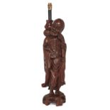 A large Chinese hardwood figural table lamp, Early 20th century, Carved as an immortal holding a ...