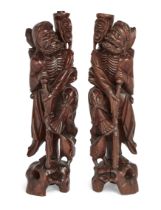 A pair of Chinese carved hardwood figural lamp bases, Early 20th century, Each carved as an emaci...