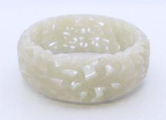 A wide pierced celadon jade bangle. Approximately 5.5 cm internal diameter.